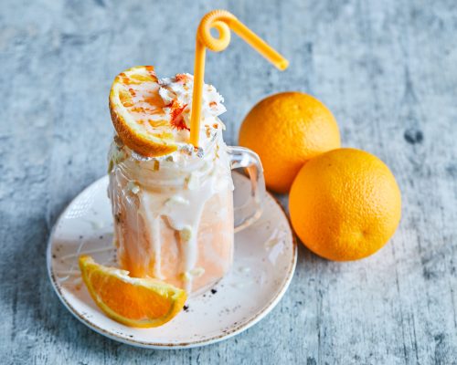 Orange smoothie with sprinkles and straw on the white plate . High quality photo
